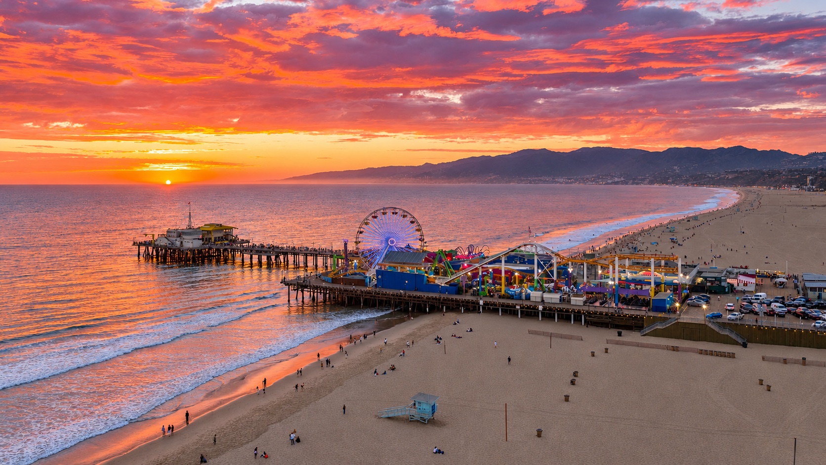 Sunset over Santa Monica Beach and Pier, with the Ferris wheel and mountains along the coast